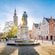 A historical town square with gabled buildings, a statue and a steeple
